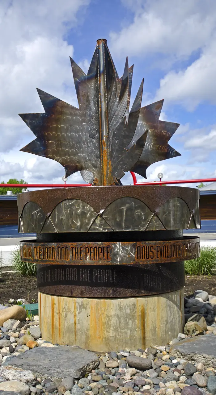 The large Legacy Prayer Drum sculpture, topped with a metal maple leaf, outdoors in Prince George