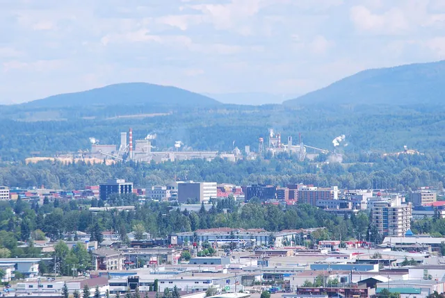 View of downtown Prince George from University Way, with low-rise buildings, trees and hills beyond